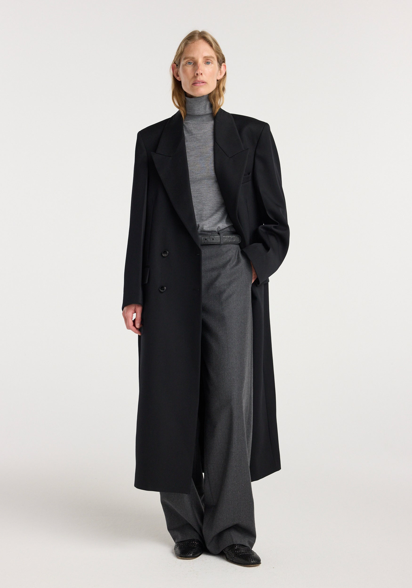 Model wearing a black double breasted tailored coat over a gray turtleneck and wide-leg trousers, showcasing a sleek and sophisticated outfit with the Double breasted tailored coat | black.