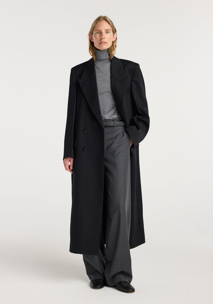 Model wearing a black double breasted tailored coat over a gray turtleneck and wide-leg trousers, showcasing a sleek and sophisticated outfit with the Double breasted tailored coat | black.
