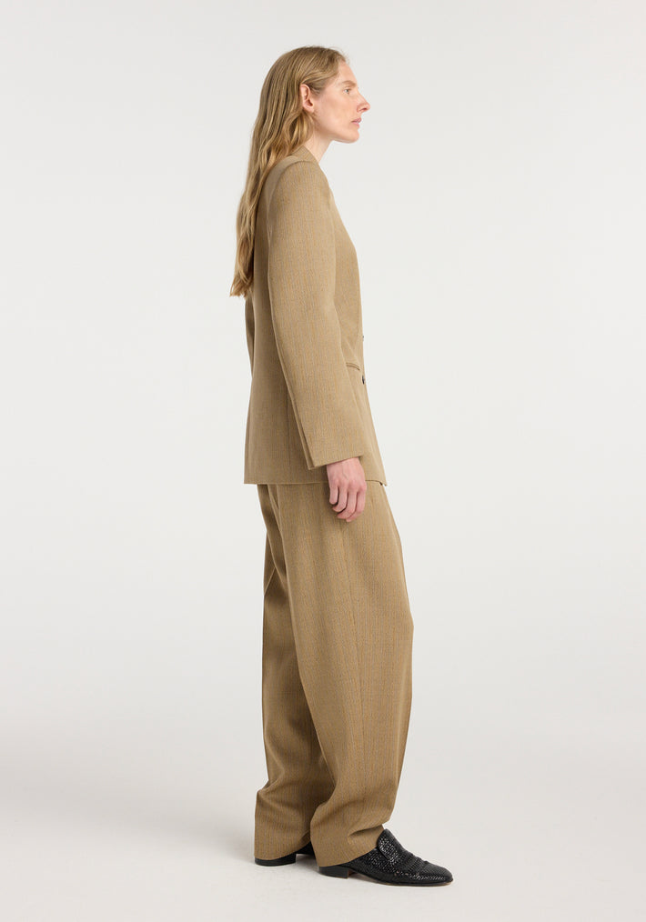 Side profile of a model wearing an Overlap lapel blazer | heritage stripe in a tan color with matching wide-leg trousers and black shoes against a plain background.