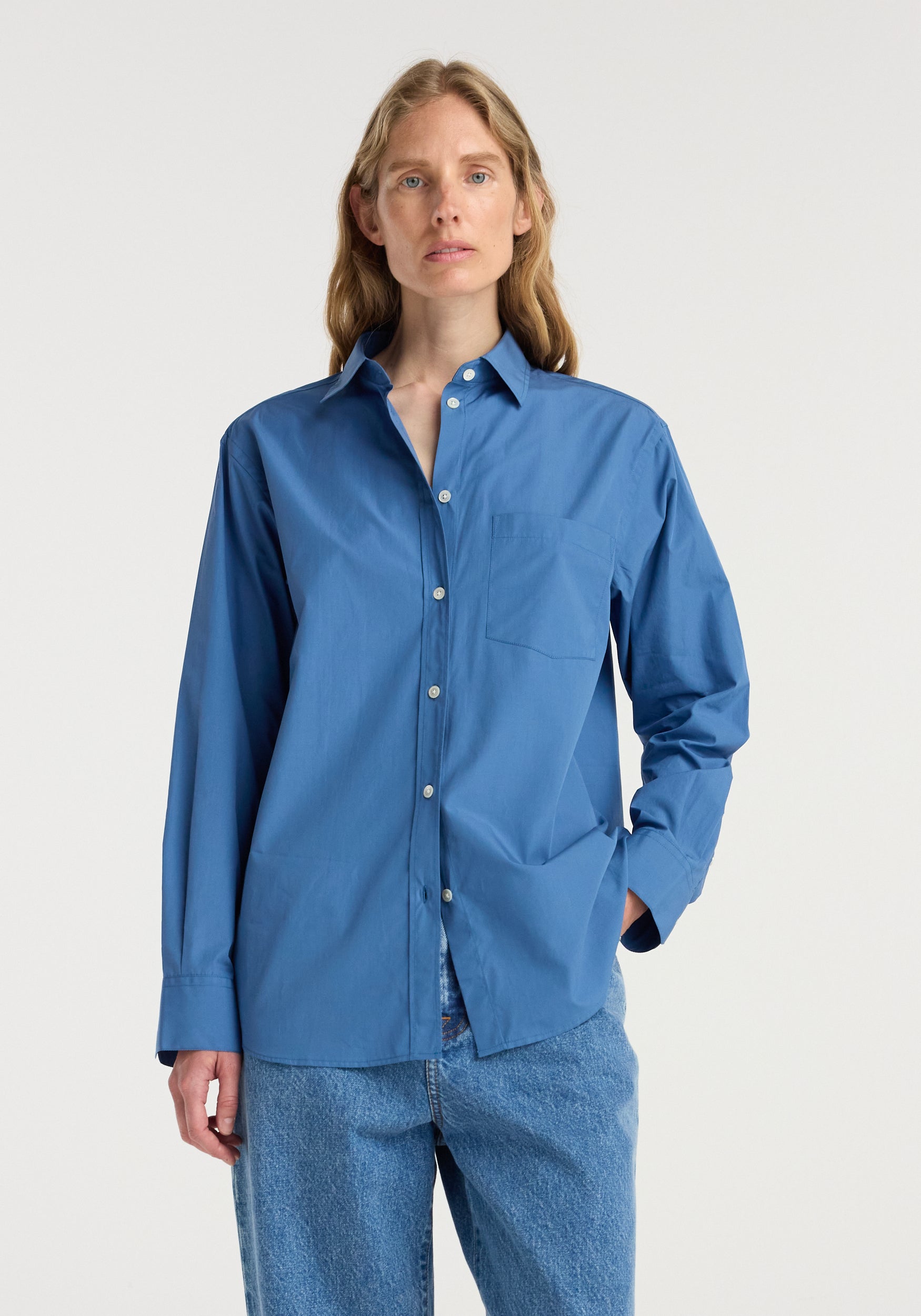 Woman wearing a classic fit shirt | pacific blue, styled with blue jeans, featuring a button-down front and chest pocket in a relaxed fit.