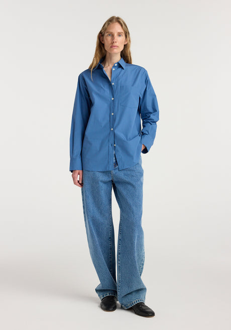 Woman wearing a blue long-sleeve button-up shirt paired with loose-fitting jeans and black shoes, styled to display the Classic fit shirt | pacific blue.