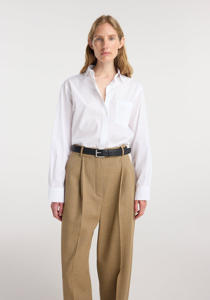 Woman wearing a Classic fit shirt | optic white with long sleeves and a front pocket, paired with high-waisted tan pleated trousers and a black belt against a plain background.