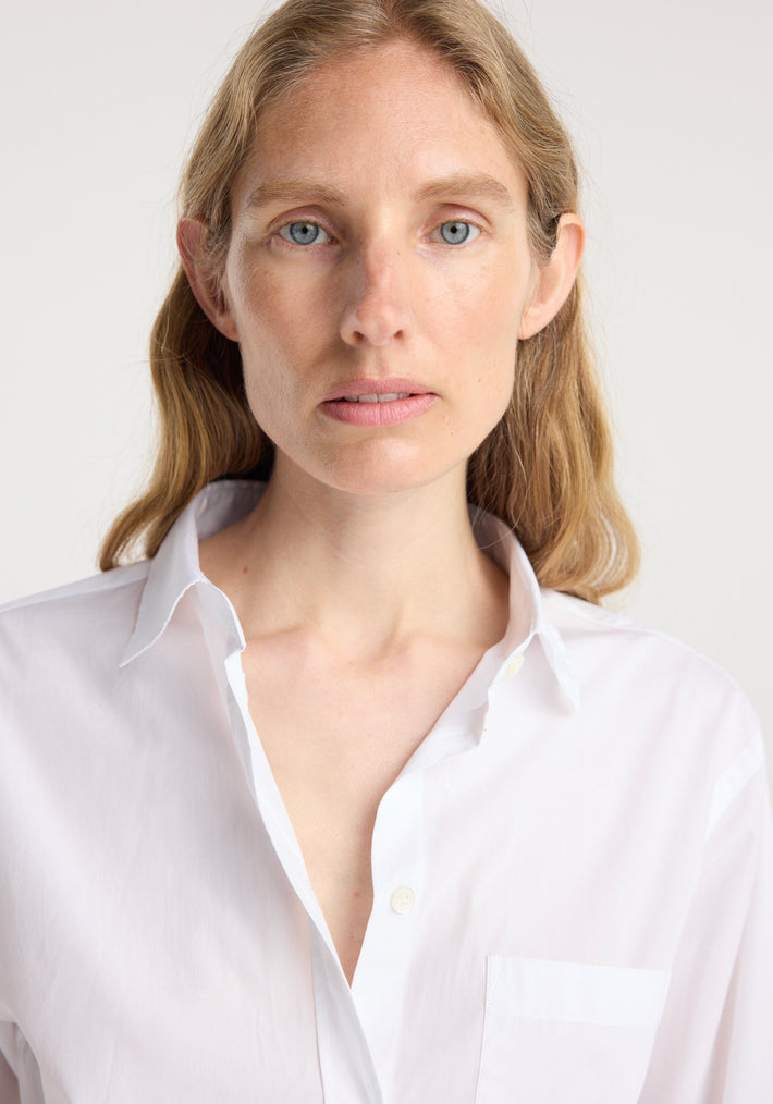 Close-up of a woman wearing a classic fit shirt | optic white with a slightly open collar and chest pocket, showcasing the clean and crisp fabric texture.
