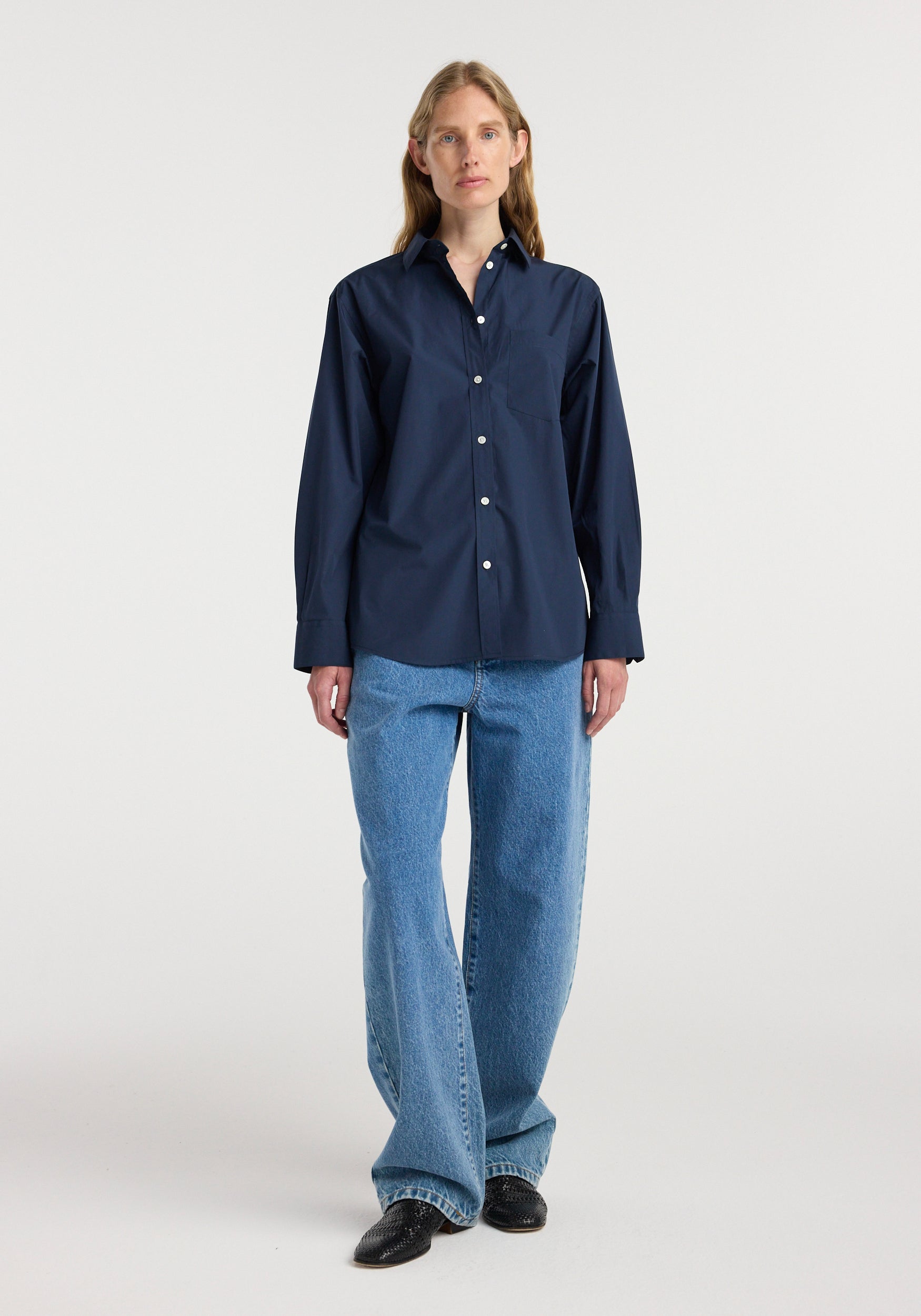 Woman wearing a navy long-sleeve button-up Classic fit shirt | navy paired with light blue wide-leg jeans and black shoes, standing against a plain white background.