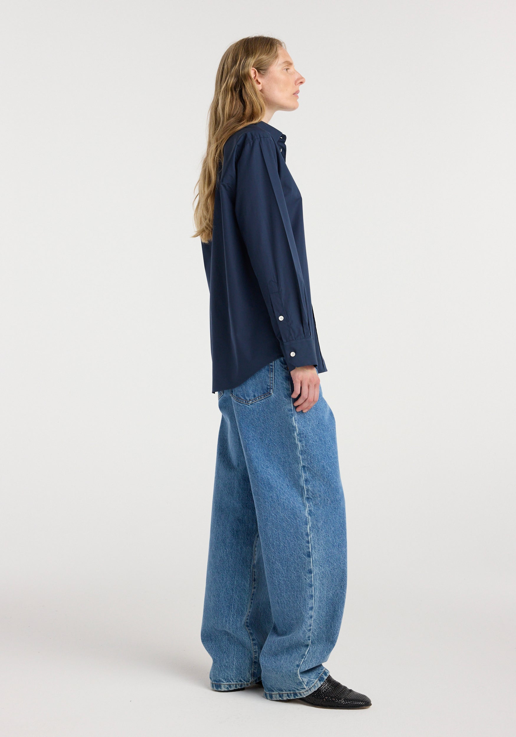 Side view of a woman wearing a navy long-sleeve Classic fit shirt | navy paired with loose-fitting blue jeans and black pointed shoes against a plain background.