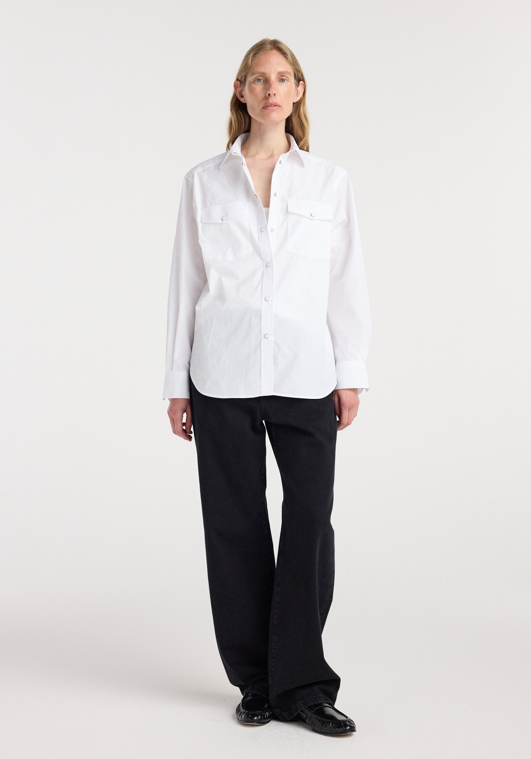 Woman wearing a white long-sleeve Western shirt | optic white with buttoned flap pockets on the chest, styled with black pants and black shoes against a plain background.