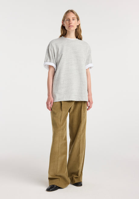 Woman wearing a Japanese mouliné jersey t-shirt | grey mouliné with a loose fit and rolled sleeves, paired with wide-leg beige corduroy pants and black shoes against a white background.