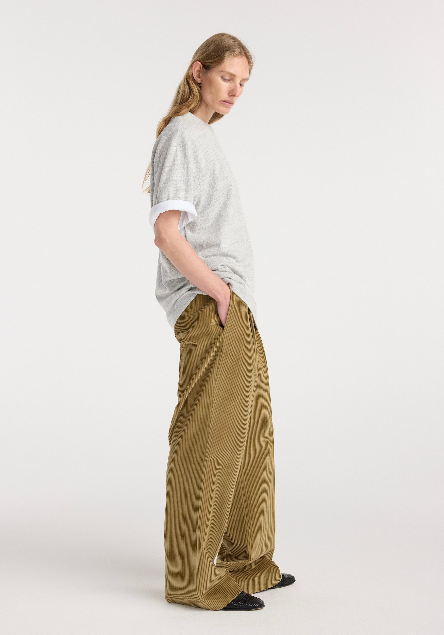Side view of a woman wearing a grey textured short-sleeve top layered over a white shirt and loose-fitting brown corduroy pants, styled with black shoes, showcasing the Japanese mouliné jersey t-shirt | grey mouliné.