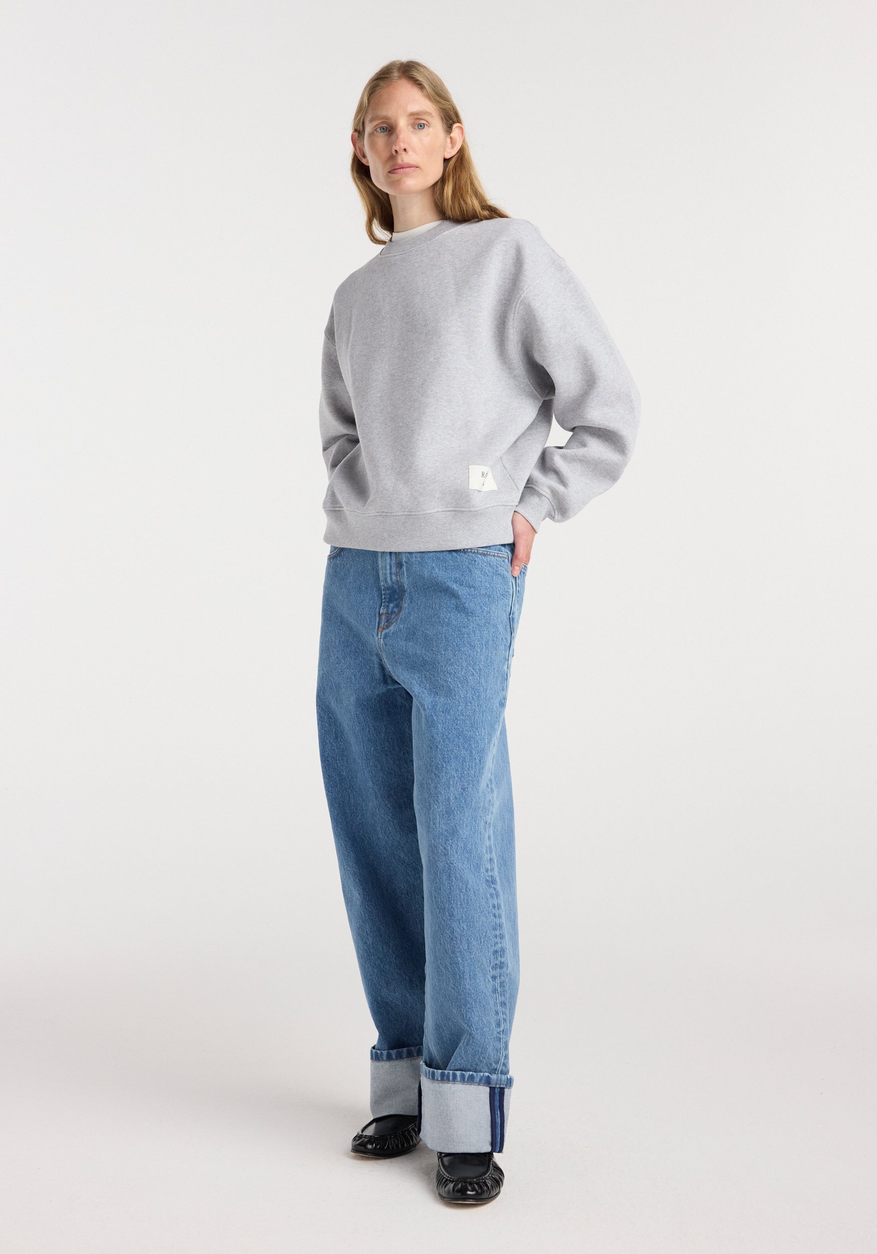 Woman wearing a Sweatshirt | mid grey melange with a relaxed fit, paired with rolled-up wide-leg blue jeans and black shoes, standing against a plain white background.
