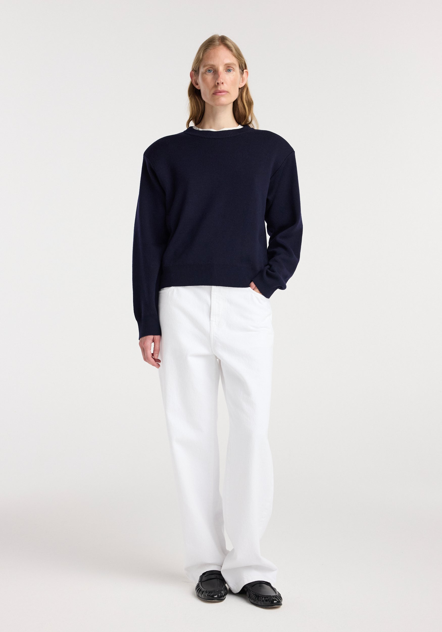 Model wearing a navy blue Statement shoulder crewneck | navy sweater paired with white pants and black shoes, standing against a plain white background.