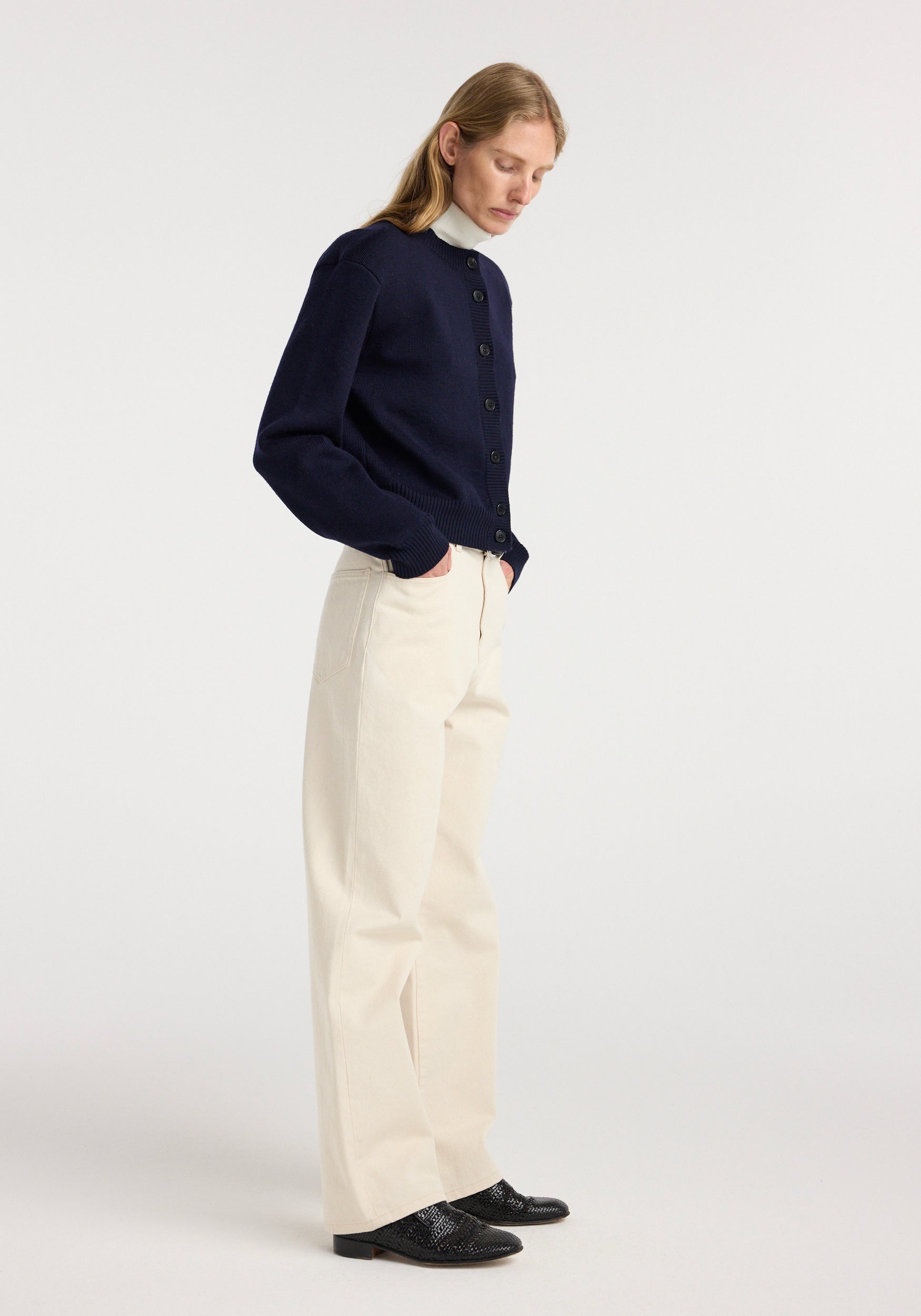 Woman wearing a navy Statement shoulder cardigan | navy with button-up front, paired with cream wide-leg pants and black textured shoes, standing against a plain background.