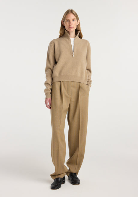 Woman wearing a camel-colored zipped mouliné polo with a high collar and long sleeves, paired with matching wide-leg trousers and black shoes, standing against a plain background.