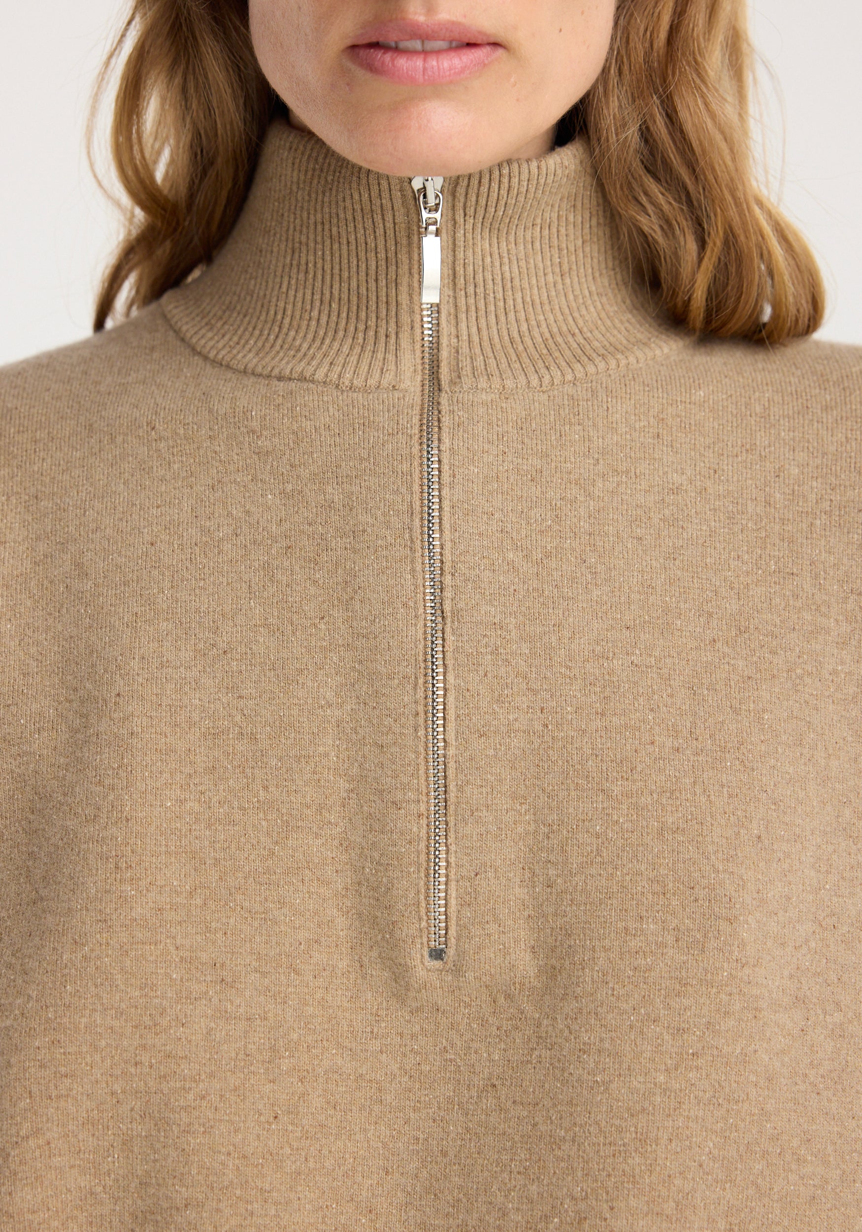 Close-up of a person wearing a zipped mouliné polo | camel featuring a high ribbed collar and a silver zipper down the front center.