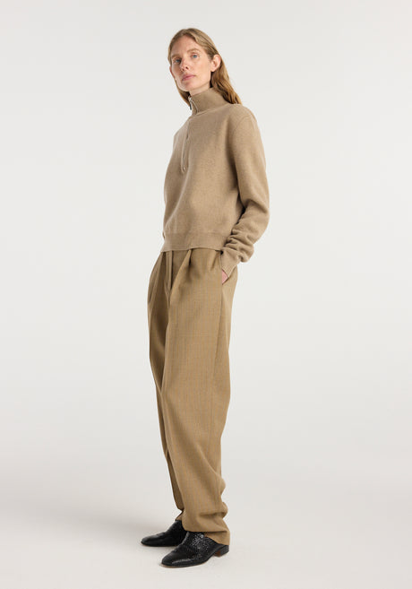 A model wearing beige single pleat tapered trousers with a subtle heritage stripe pattern paired with a light brown zip-up sweater and black shoes, showcasing Daria - Single pleat tapered trousers | heritage stripe.