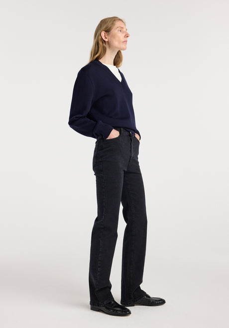 Woman wearing Lino - High-rise straight denim | black paired with a navy blue v-neck sweater and black shoes, standing against a plain white background.