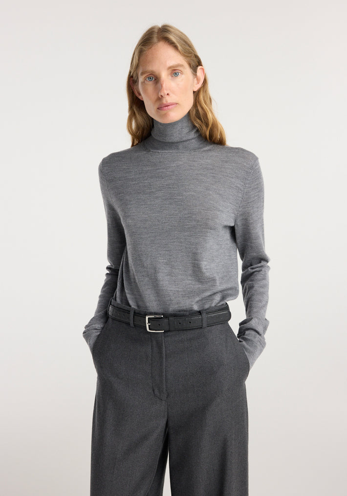 Woman wearing wide leg trousers | dark grey melange paired with a grey turtleneck sweater and black belt, standing against a plain light background.