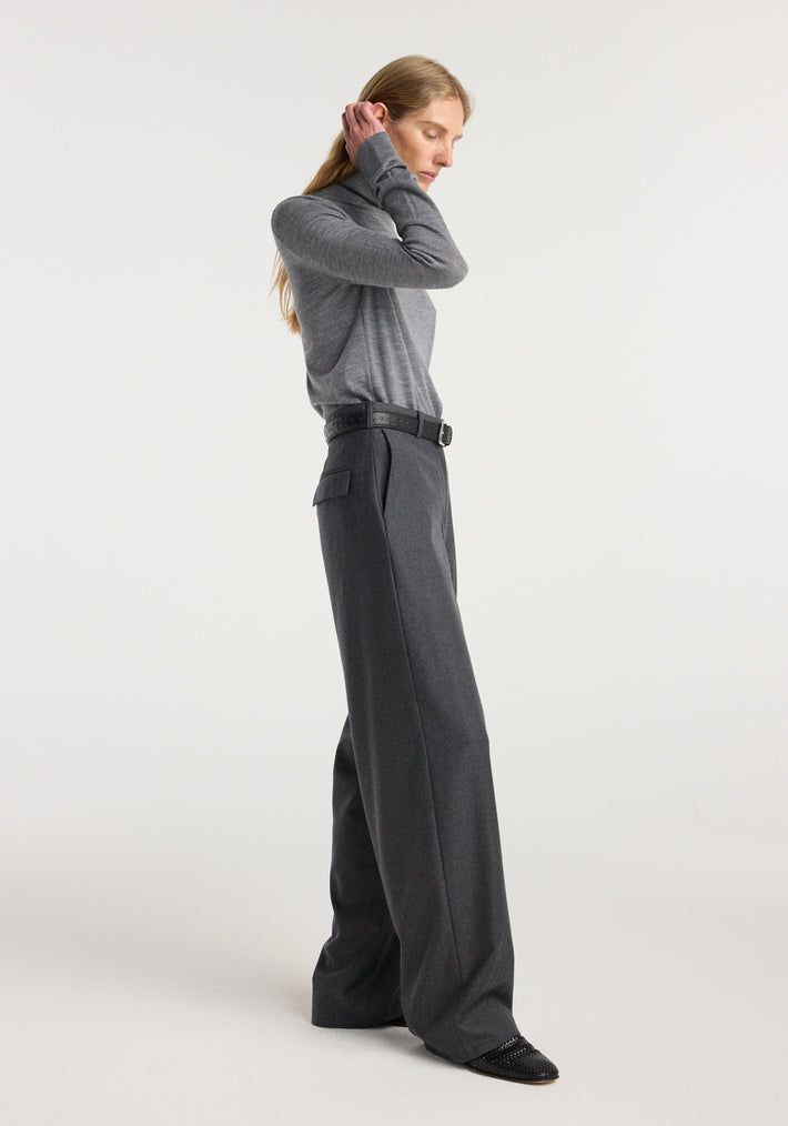 Woman wearing wide leg trousers | dark grey melange paired with a grey long-sleeve top and black belt, standing in a side profile pose against a white background.