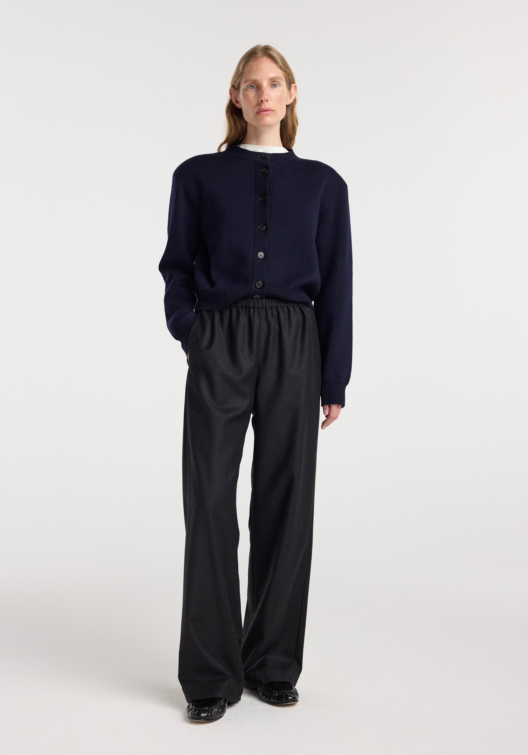 A model wearing relaxed fit trousers | anthracite melange paired with a dark navy button-up sweater and black shoes, standing against a plain white background.