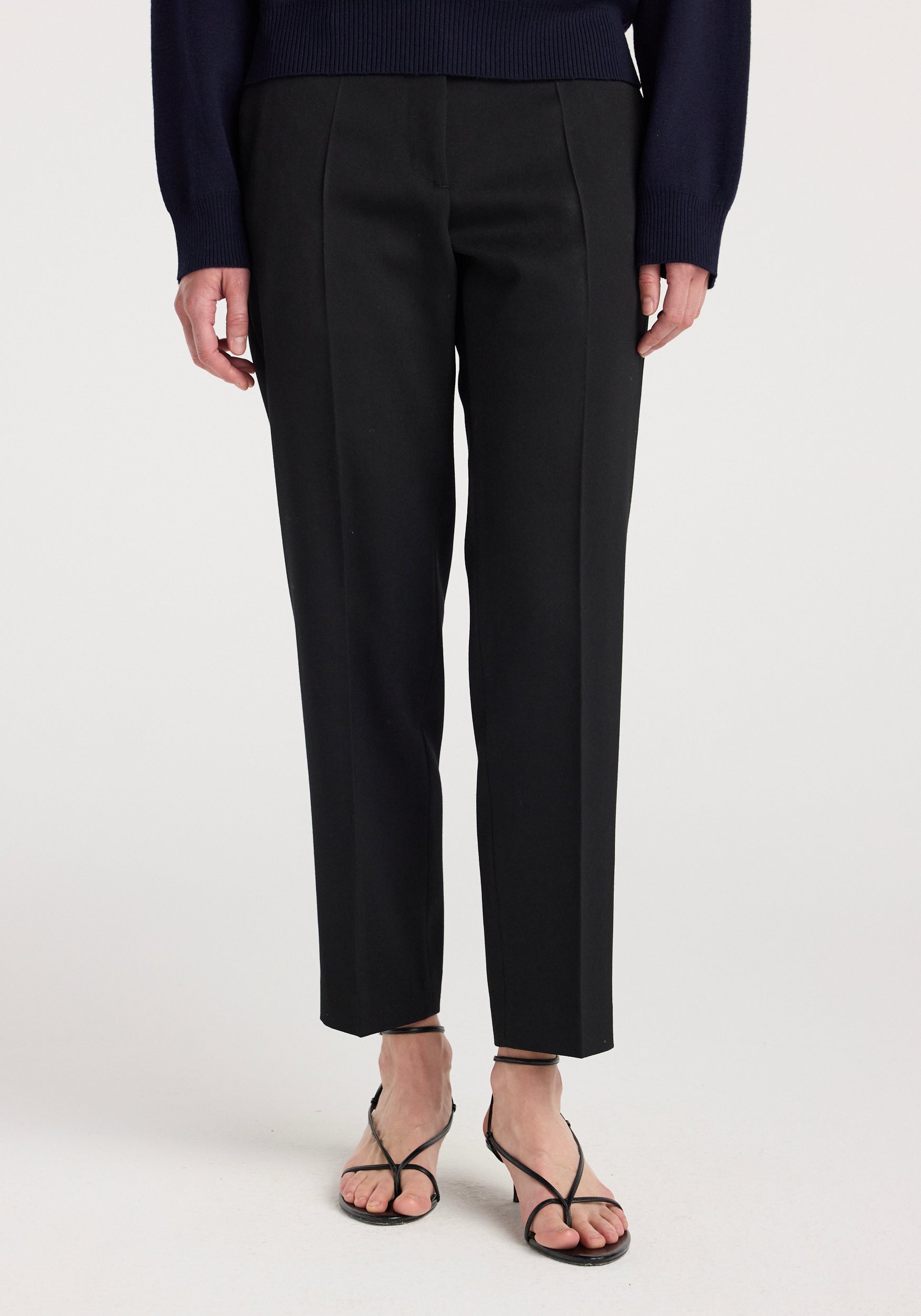 Front view of a person wearing Mies - Cigarette leg tailored trousers | black paired with black strappy sandals and a navy sweater.