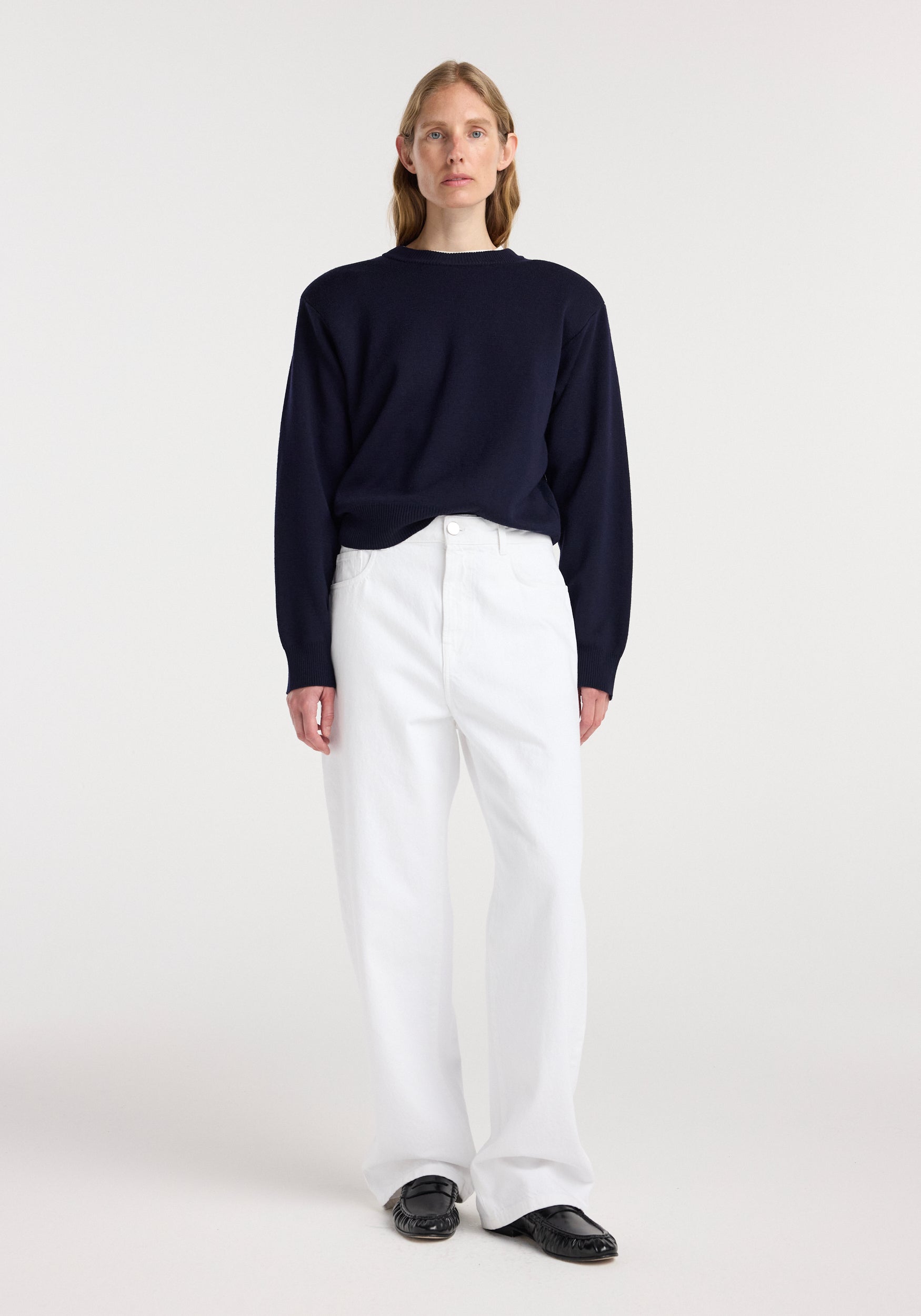 Model wearing Bruun - Signature baggy denim | optic white paired with a navy long-sleeve top and black shoes, standing against a plain white background.