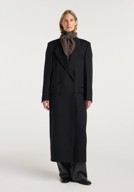 Model wearing a Small knitted triangle scarf | brown melange tied neatly around the neck paired with a long black coat and gray pants.