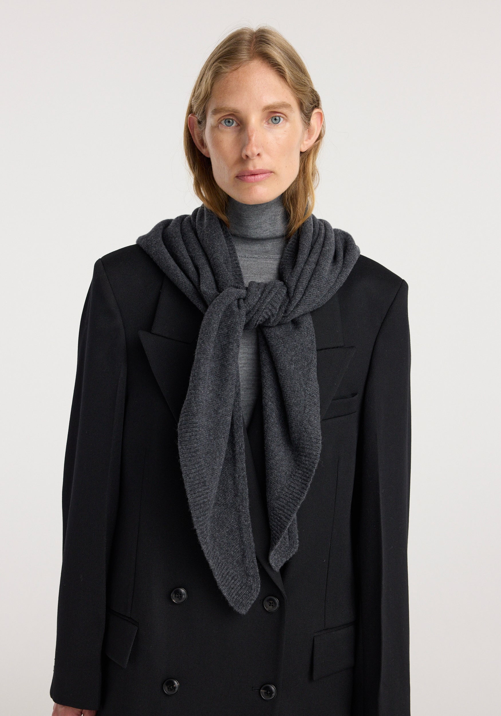 Woman wearing a large knitted triangle scarf | anthracite melange draped and tied loosely around her neck over a dark coat and turtleneck sweater.