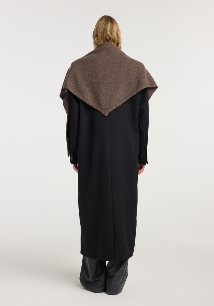 Back view of a person wearing a Large knitted triangle scarf | brown melange draped over a long black coat against a plain white background.