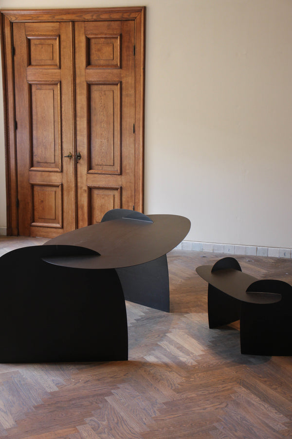Sculpted Table | 9845: Two minimalist, matte-black, abstract bench-like pieces crafted from sustainably harvested oak by Arne Kristian, displayed in a gallery-like room with herringbone flooring.