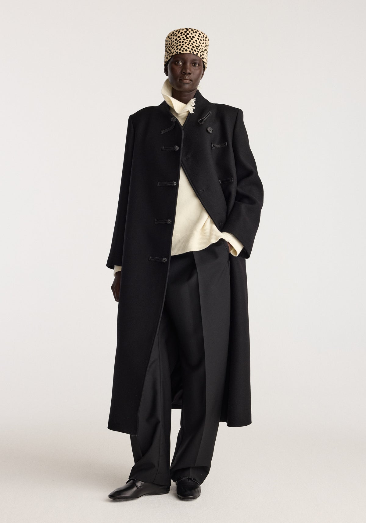 Cheetah leather hat | cheetah worn by a model with a black tailored coat, cream sweater, wide leg trousers and black shoes against a light background