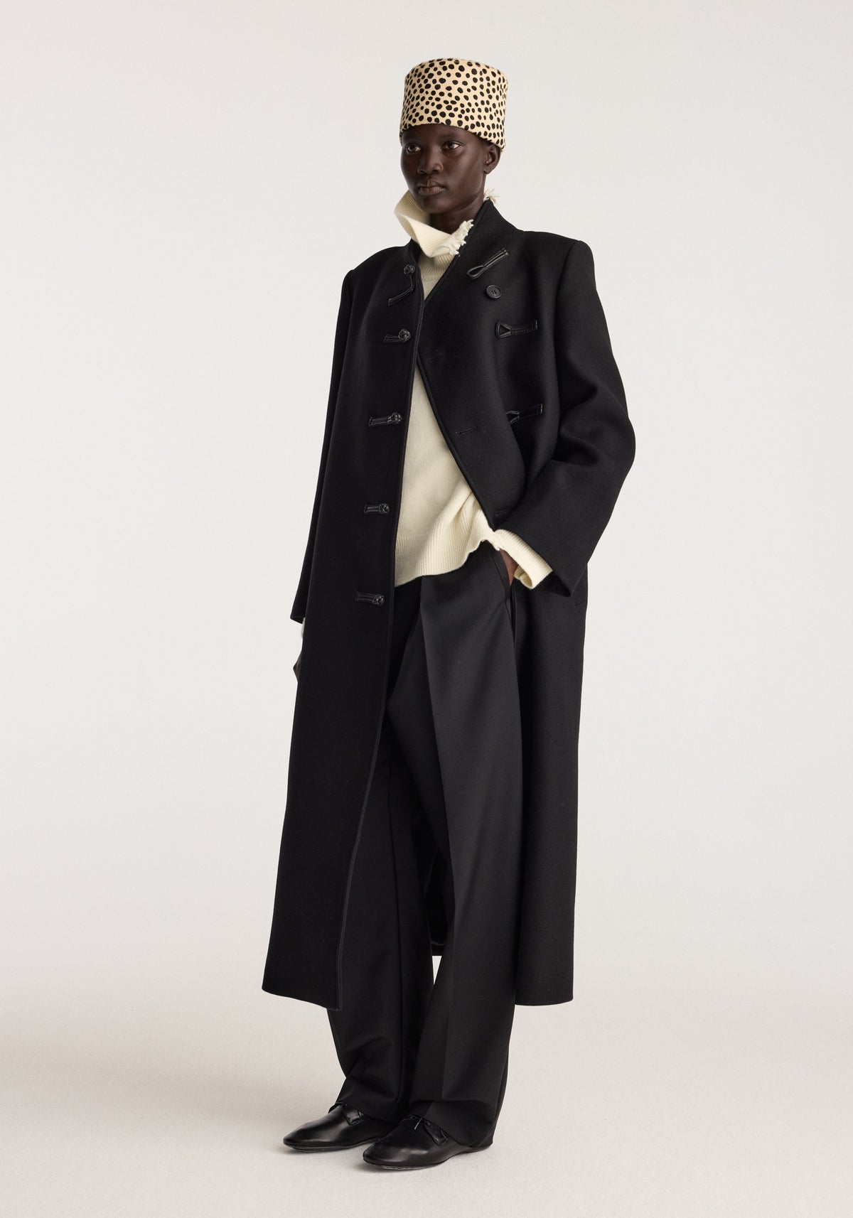 Cheetah leather hat | cheetah worn with a long black coat and wide leg trousers by a model in a studio setting