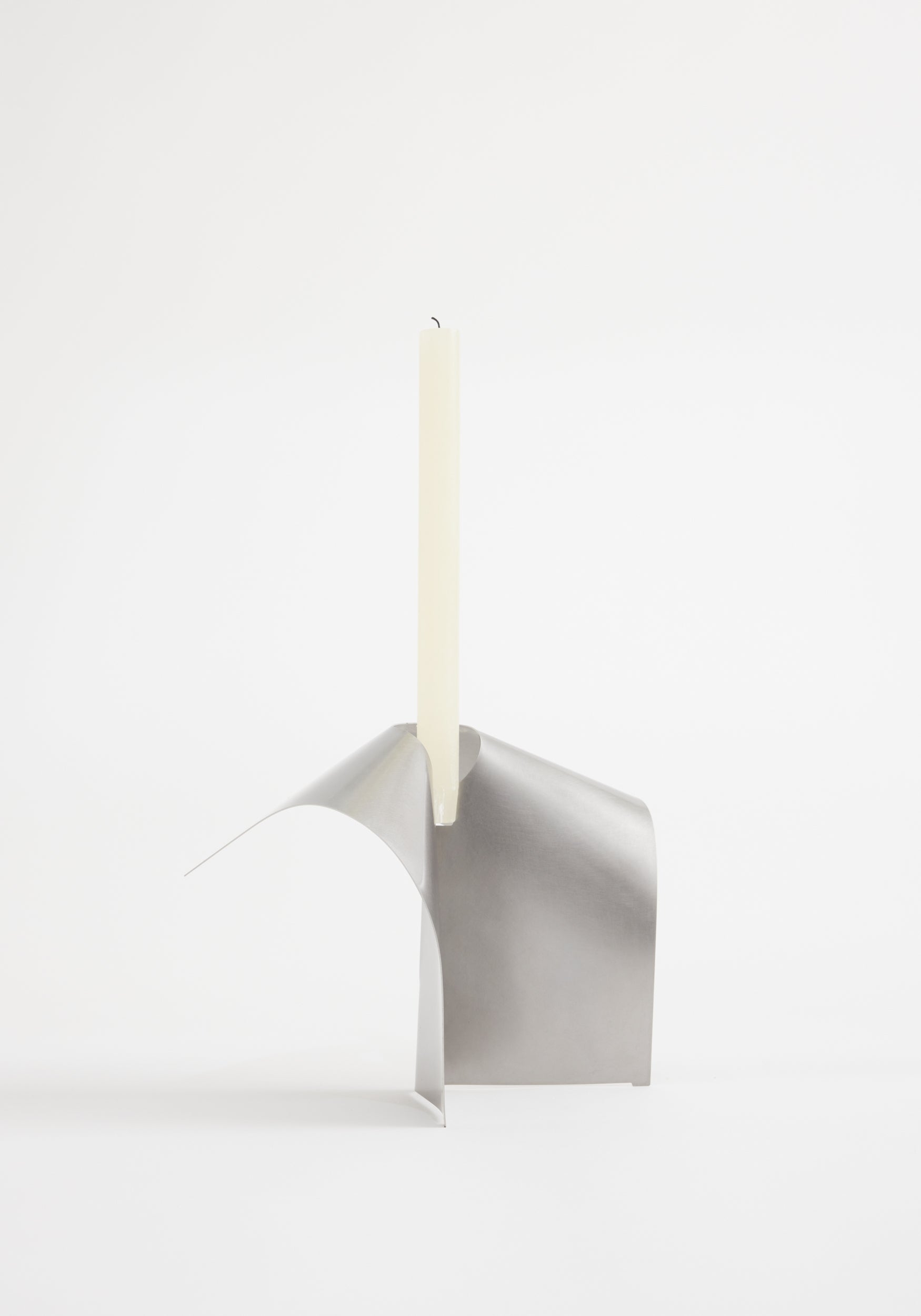 Stainless steel candle holder: Minimalist design by Paul Coenen, crafted from a single folded sheet into an S-like shape, holds an ivory taper candle.