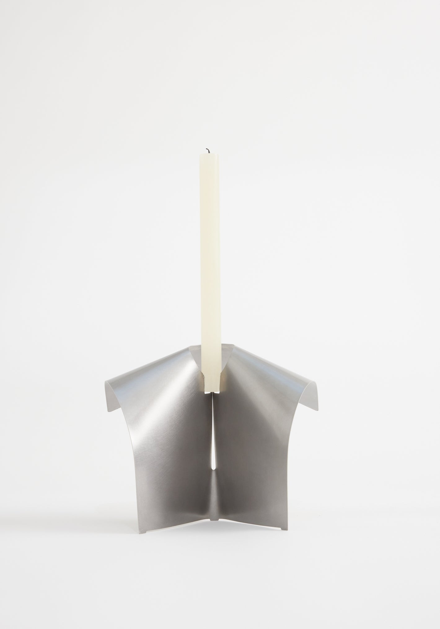 Stainless steel candle holder featuring a minimalist, tripod-like design from folded metal, securely holding an ivory taper candle. Designed by Paul Coenen, handcrafted in the Netherlands.