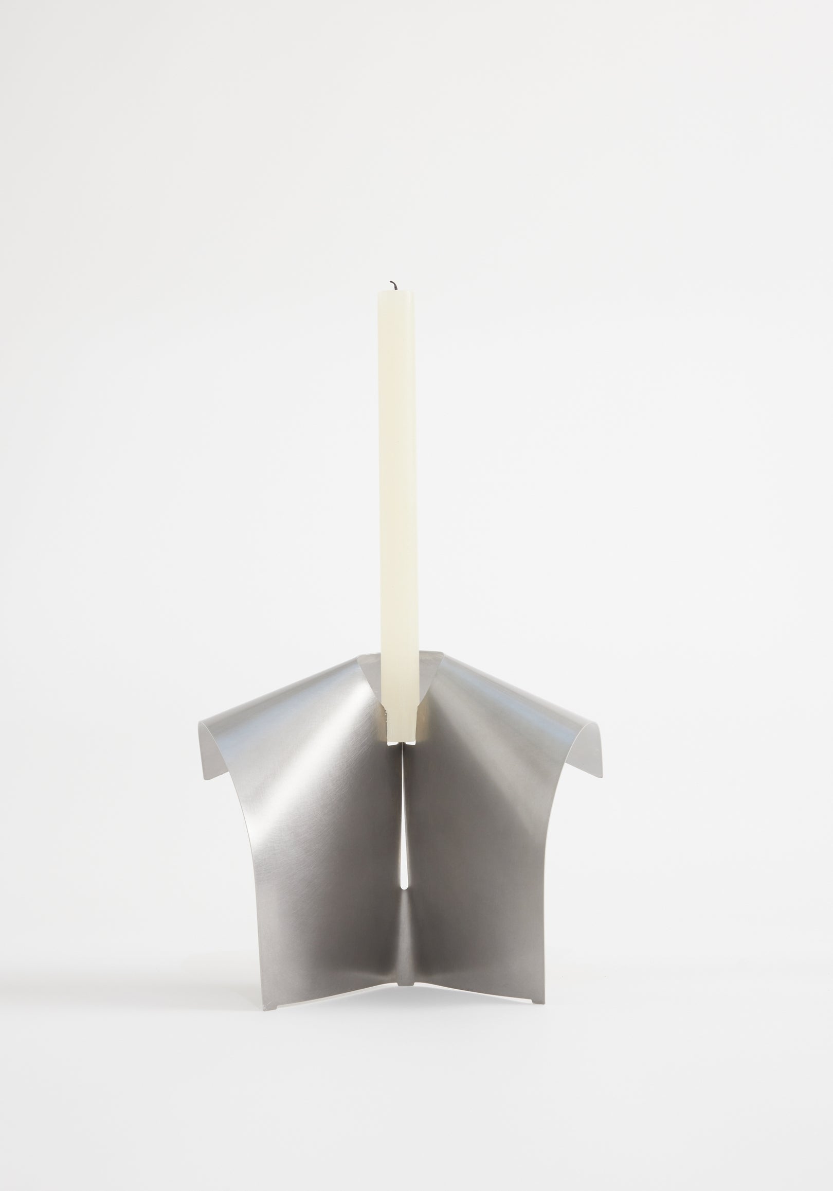 Stainless steel candle holder featuring a minimalist, tripod-like design from folded metal, securely holding an ivory taper candle. Designed by Paul Coenen, handcrafted in the Netherlands.