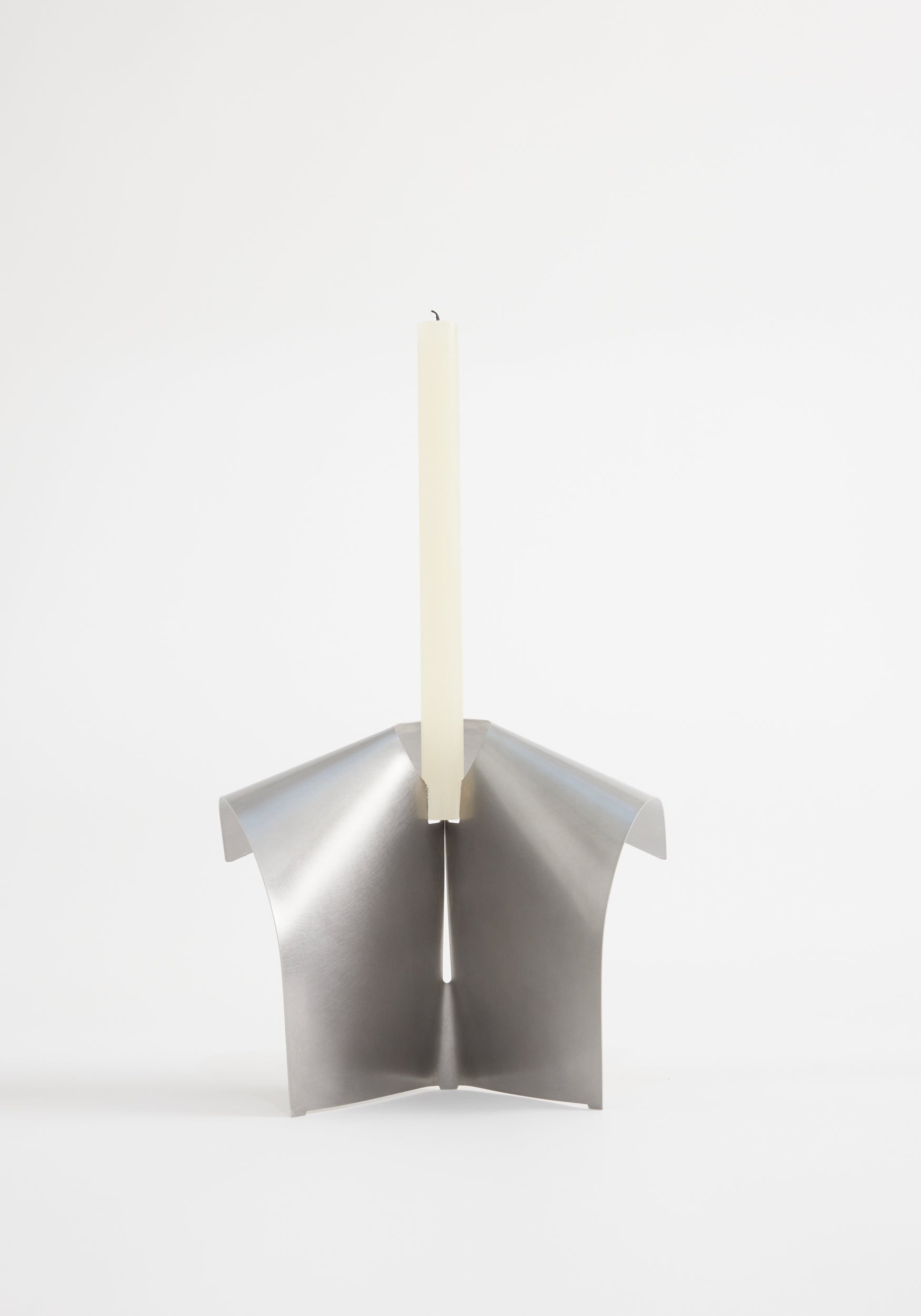 Stainless steel candle holder featuring a minimalist, tripod-like design from folded metal, securely holding an ivory taper candle. Designed by Paul Coenen, handcrafted in the Netherlands.