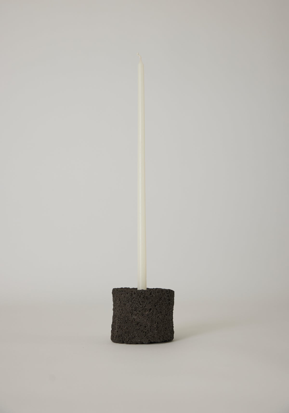 Round Candle Holder in black, crafted by Louis Crombag from lava stone, holding a white taper candle, showcasing a unique, handcrafted design.
