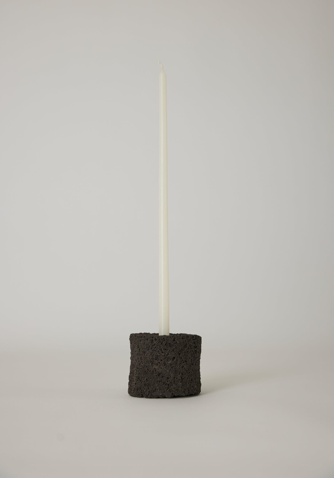 Round Candle Holder in black, crafted by Louis Crombag from lava stone, holding a white taper candle, showcasing a unique, handcrafted design.