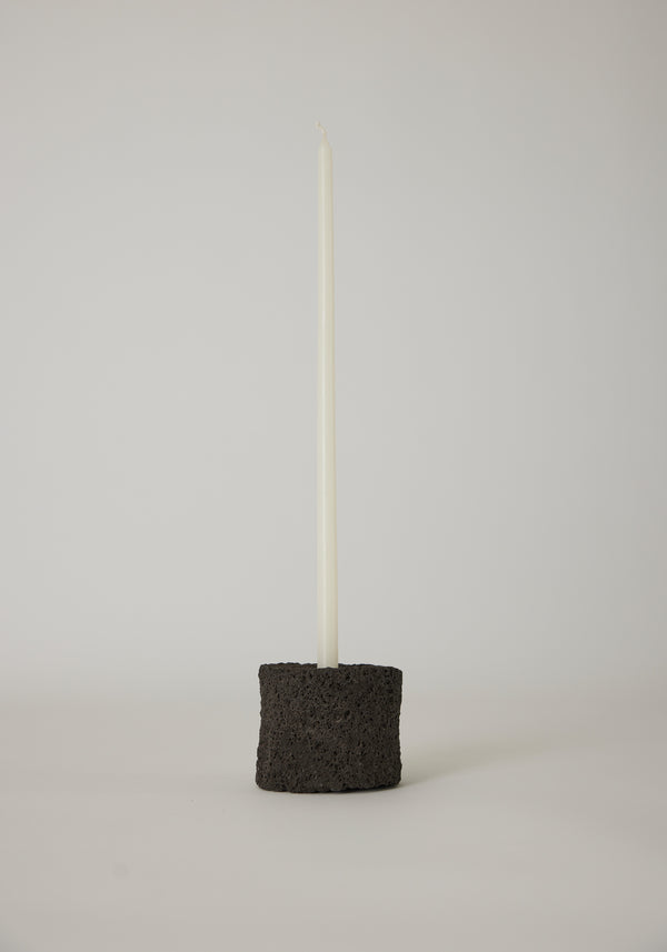 Round Candle Holder in black, crafted by Louis Crombag from lava stone, holding a white taper candle, showcasing a unique, handcrafted design.