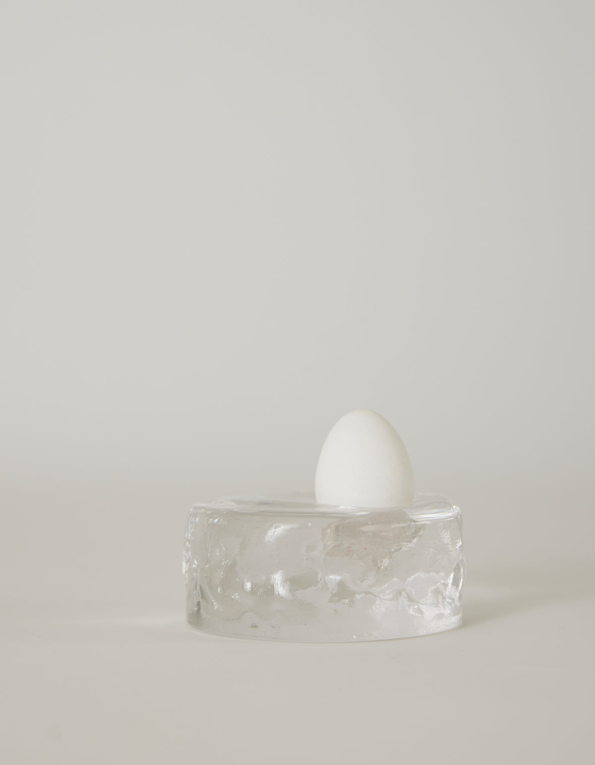 Presse-papier & holder | Glass: A white egg stands upright on a clear, textured glass block, showcasing minimalist design by Szkło Studio's unique, handcrafted approach.