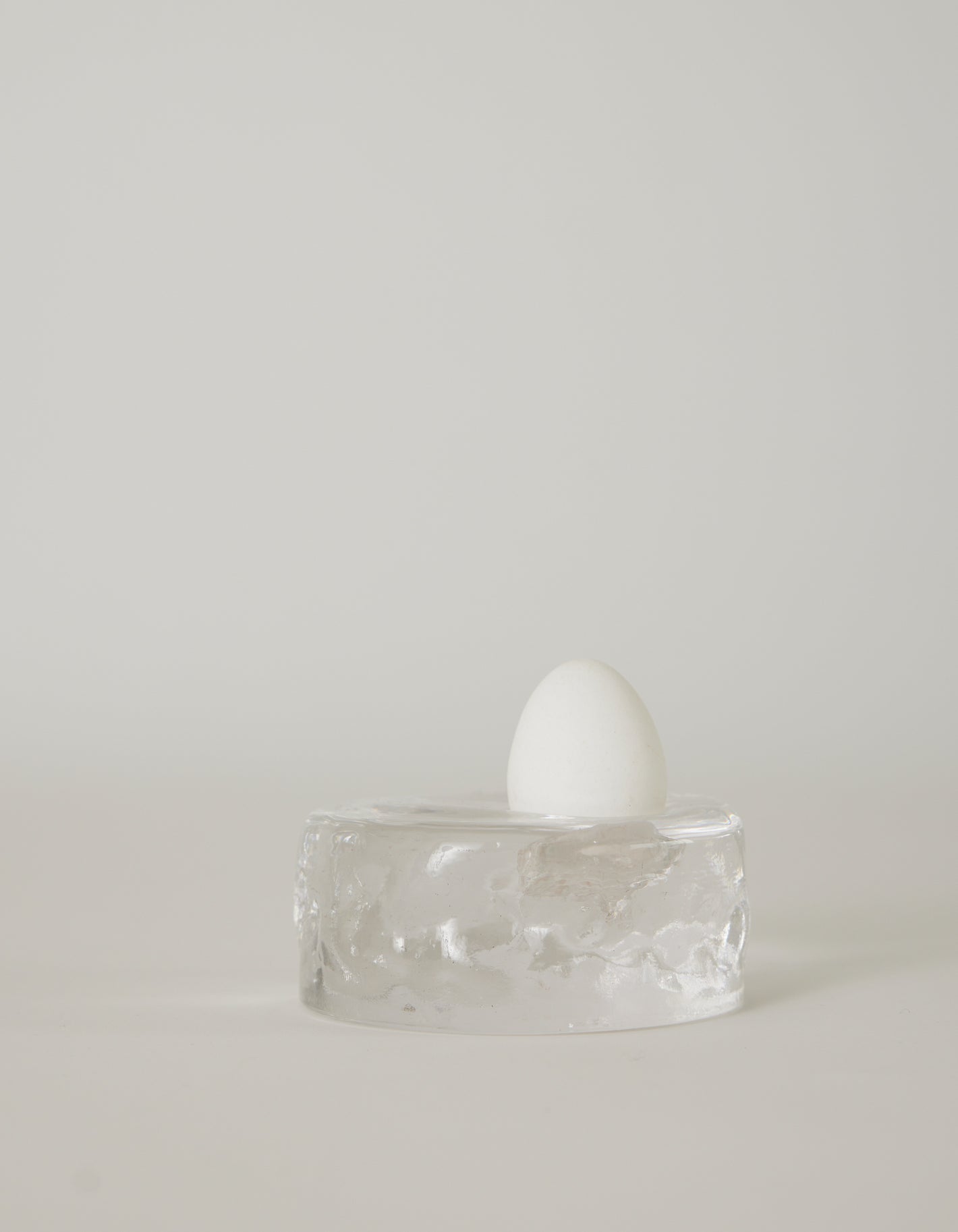 Presse-papier & holder | Glass: A white egg stands upright on a clear, textured glass block, showcasing minimalist design by Szkło Studio's unique, handcrafted approach.