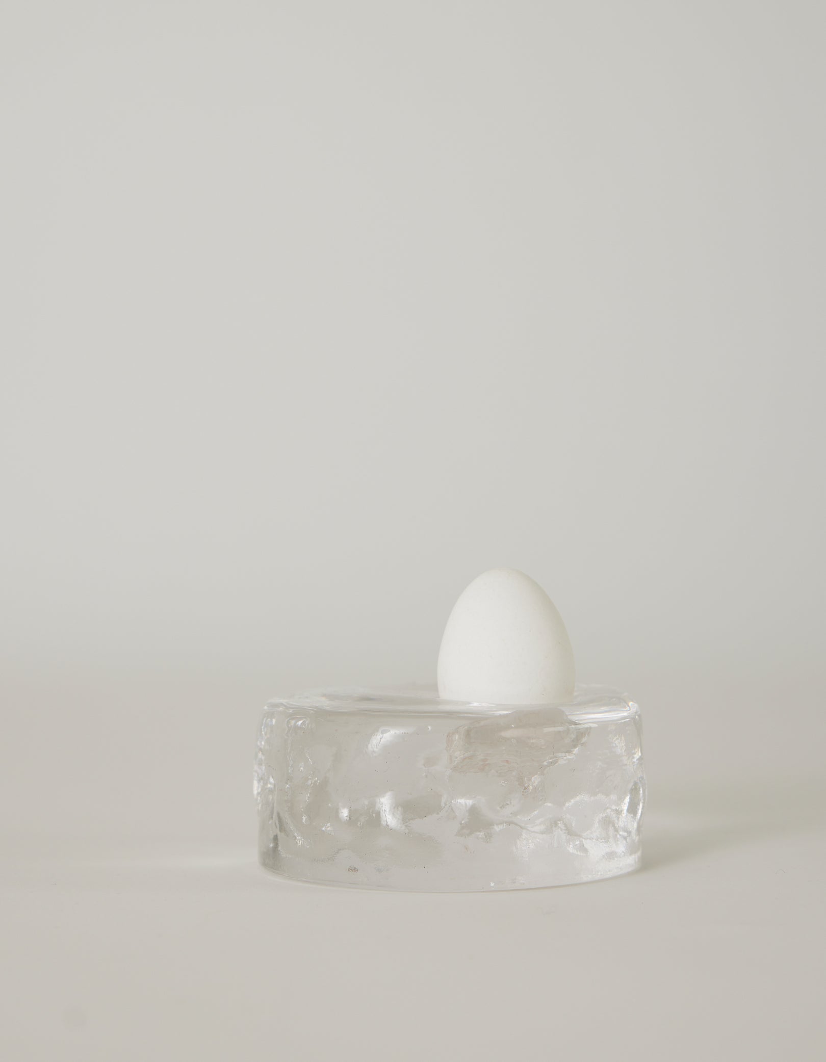 Presse-papier & holder | Glass: A white egg stands upright on a clear, textured glass block, showcasing minimalist design by Szkło Studio's unique, handcrafted approach.