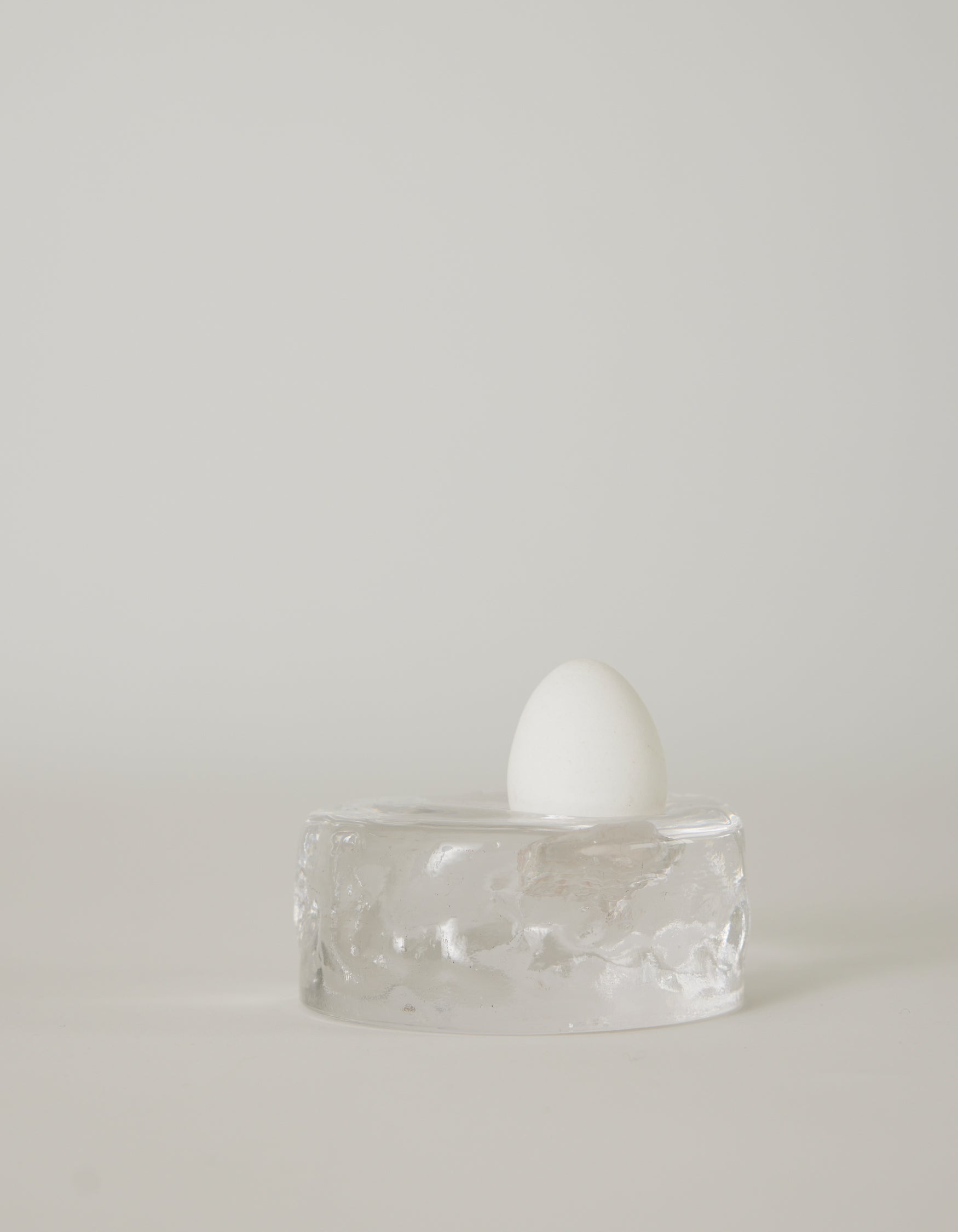 Presse-papier & holder | Glass: A white egg stands upright on a clear, textured glass block, showcasing minimalist design by Szkło Studio's unique, handcrafted approach.
