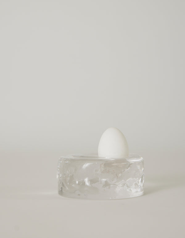 Presse-papier & holder | Glass: A white egg stands upright on a clear, textured glass block, showcasing minimalist design by Szkło Studio's unique, handcrafted approach.