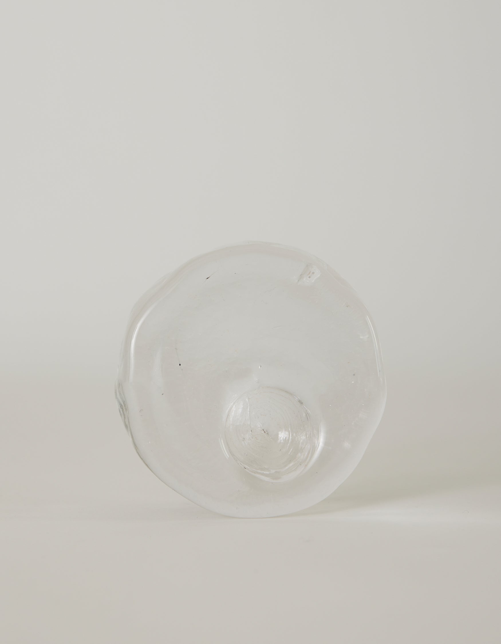 Presse-papier & holder | Glass: Hand-blown clear glass with an irregular circular shape and central dome, featuring ripples and imperfections, highlighting unique craftsmanship.