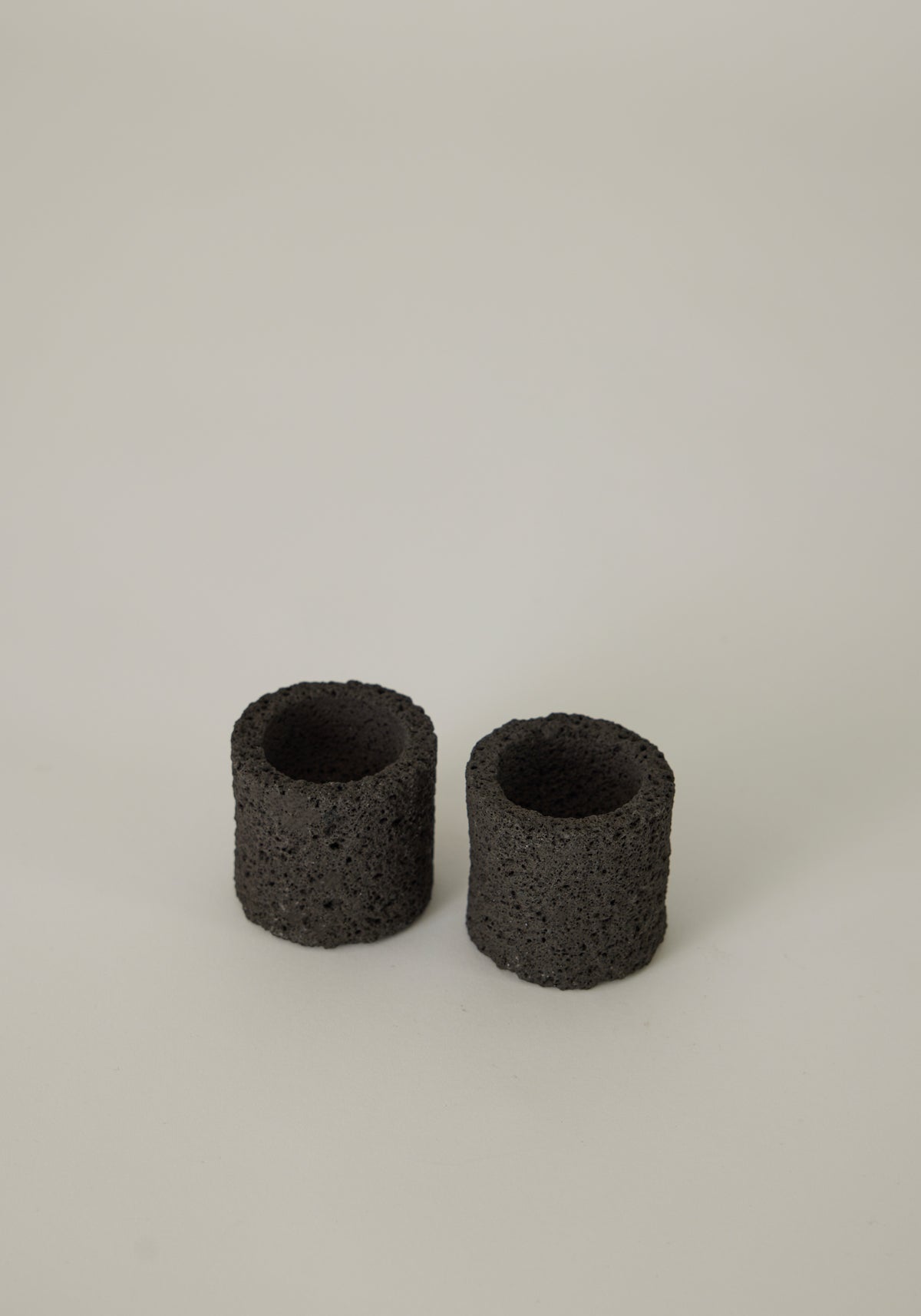 Two handcrafted Egg Cups made from dark, porous lava stone, showcasing a unique, cylindrical design, created by Dutch artist Louis Crombag.
