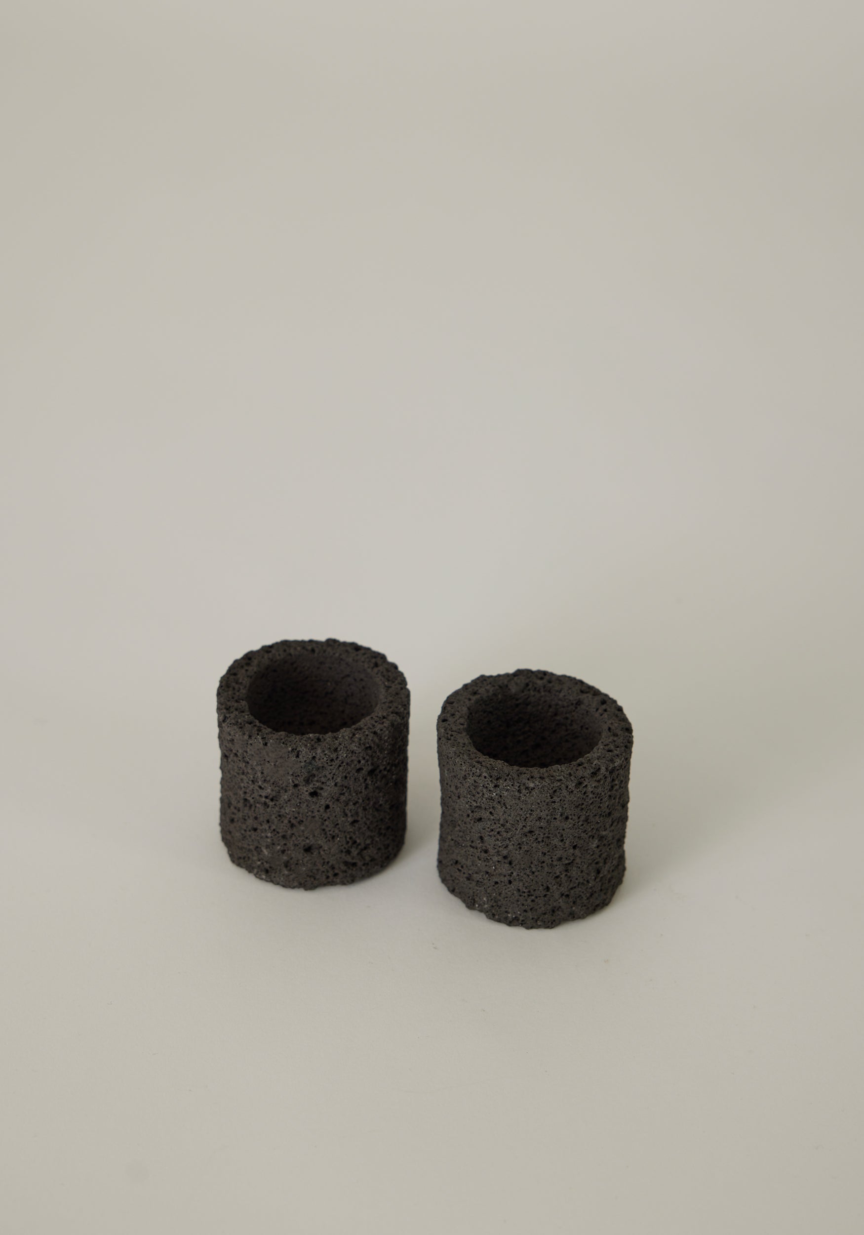 Two handcrafted Egg Cups made from dark, porous lava stone, showcasing a unique, cylindrical design, created by Dutch artist Louis Crombag.