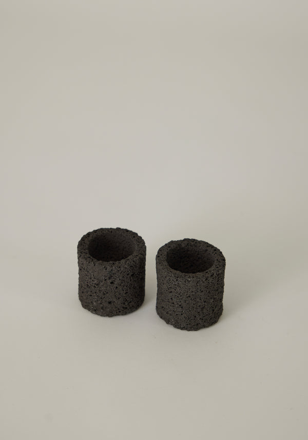 Two handcrafted Egg Cups made from dark, porous lava stone, showcasing a unique, cylindrical design, created by Dutch artist Louis Crombag.