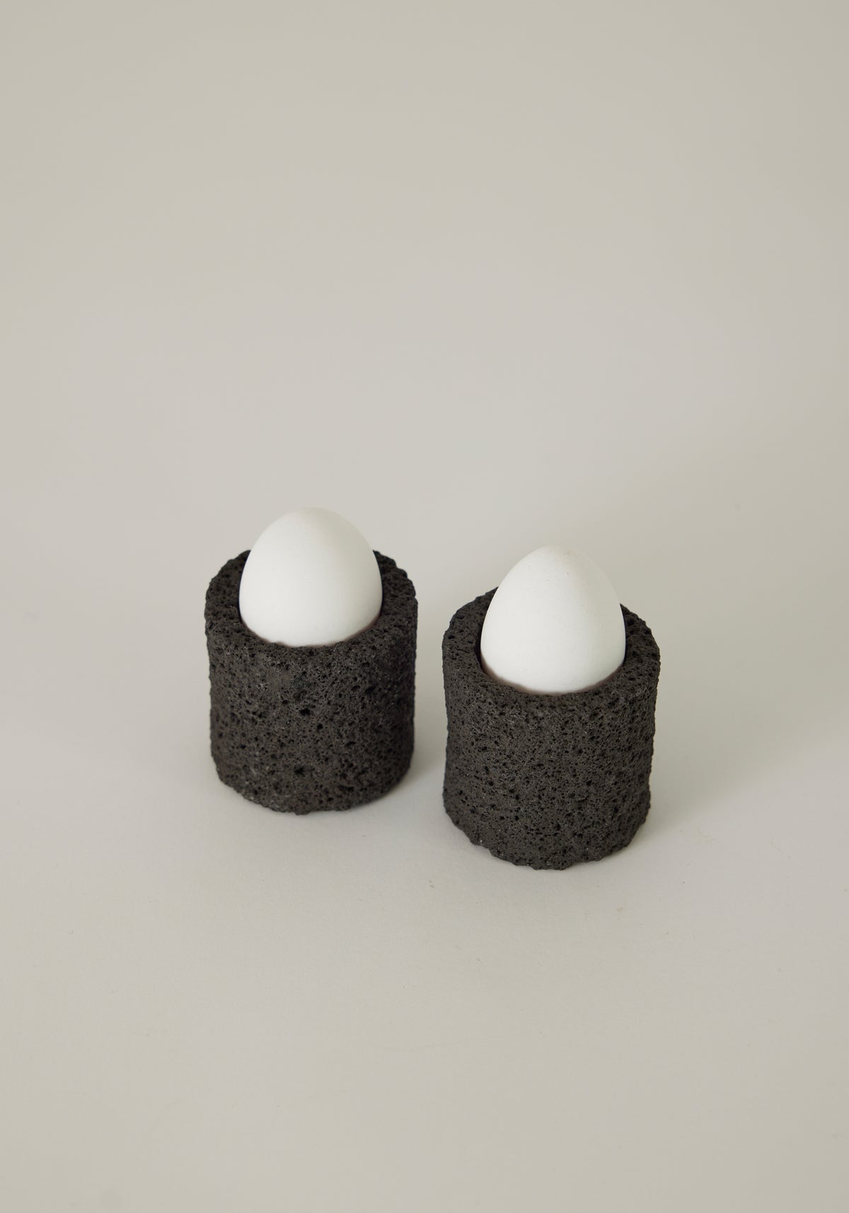 Egg Cups made from lava stone, featuring two white eggs upright in black, porous holders, handcrafted by Louis Crombag in the Netherlands.