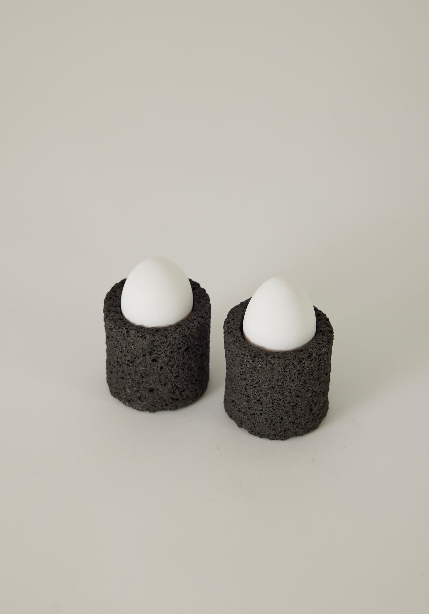 Egg Cups made from lava stone, featuring two white eggs upright in black, porous holders, handcrafted by Louis Crombag in the Netherlands.