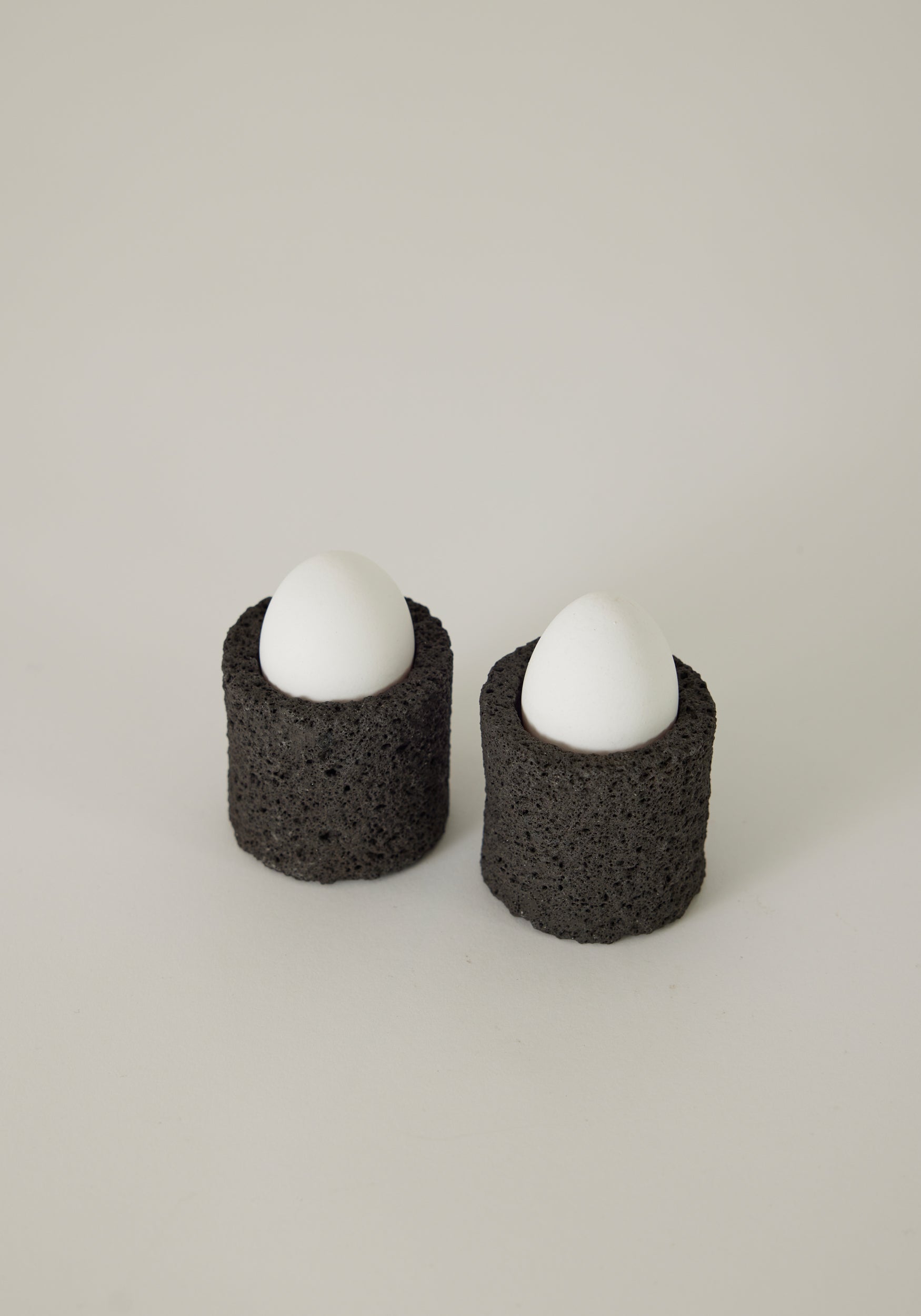 Egg Cups made from lava stone, featuring two white eggs upright in black, porous holders, handcrafted by Louis Crombag in the Netherlands.