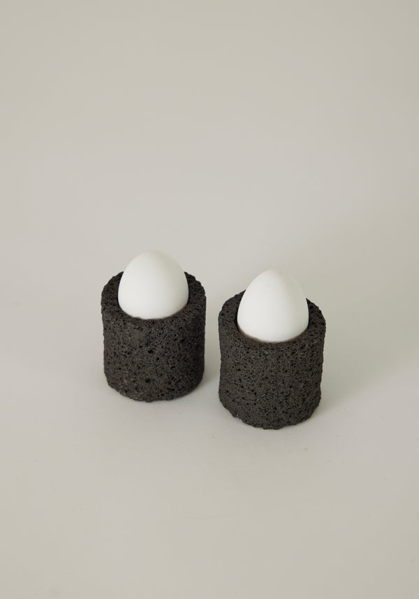 Egg Cups made from lava stone, featuring two white eggs upright in black, porous holders, handcrafted by Louis Crombag in the Netherlands.